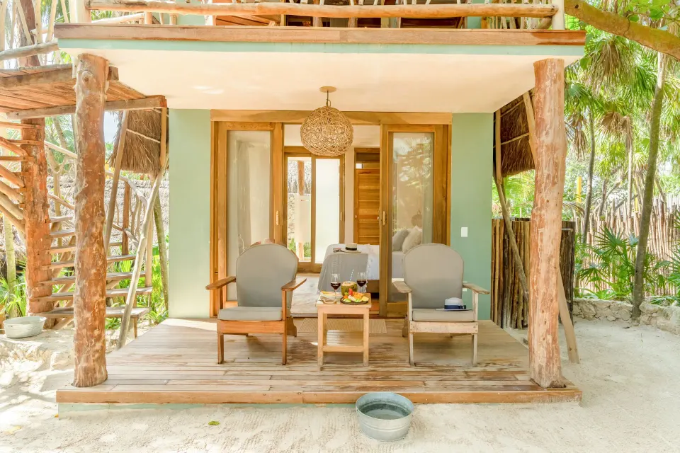 Front view of a Deluxe Room at Ahau Tulum showing the porch with two chairs and a small table