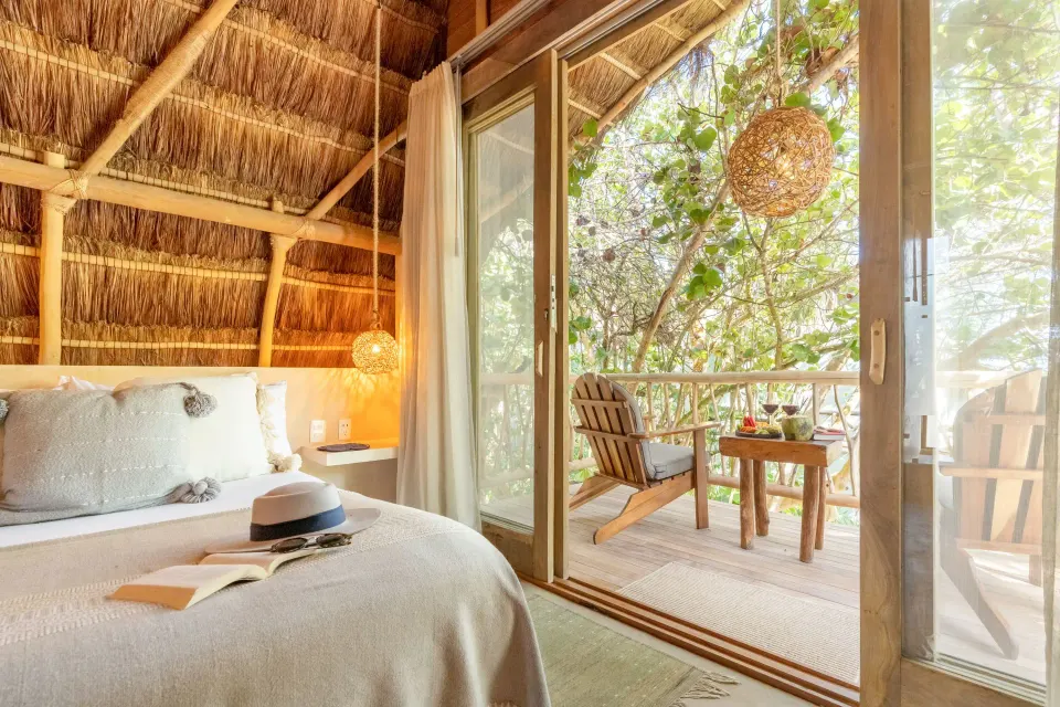 Interior of Deluxe Room at Ahau Tulum with king bed and thatched roof opening onto a small balcony