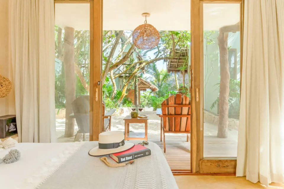 Deluxe Room at Ahau Tulum with king bed and sliding doors opening to a shaded deck and garden.