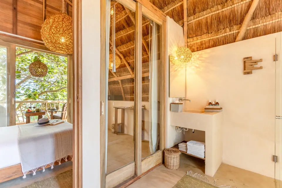 Bathroom sink area in a Deluxe Room at Ahau Tulum with shelves of folded towels and woven pendant lights