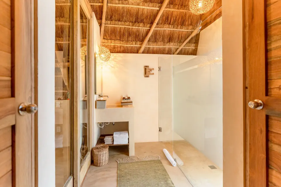 Spacious walk-in shower with glass panels and natural-fiber mats in a Deluxe Room at Ahau Tulum