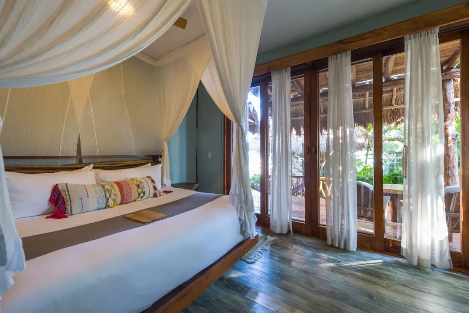 Canopy king bed beside floor-to-ceiling doors opening to the terrace at Ahau Tulum