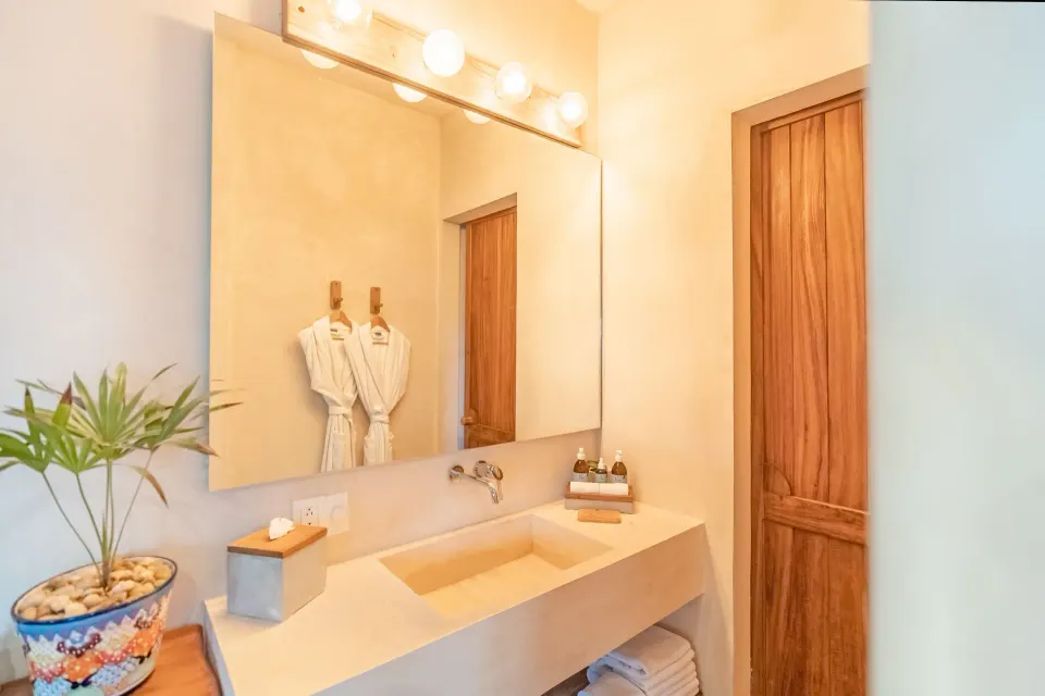 Bathroom vanity with mirror, robes and stacked towels in the junior suite at Ahau Tulum