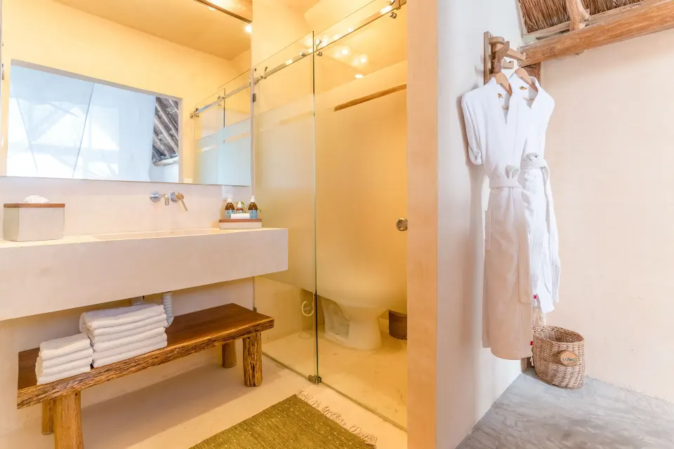 Bathroom sink, glass shower and hanging robes in the Junior Suite at Ahau Tulum
