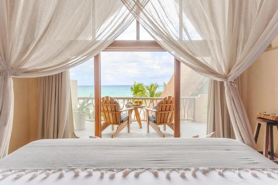 Canopy king bed framing ocean view and balcony at Ahau Tulum