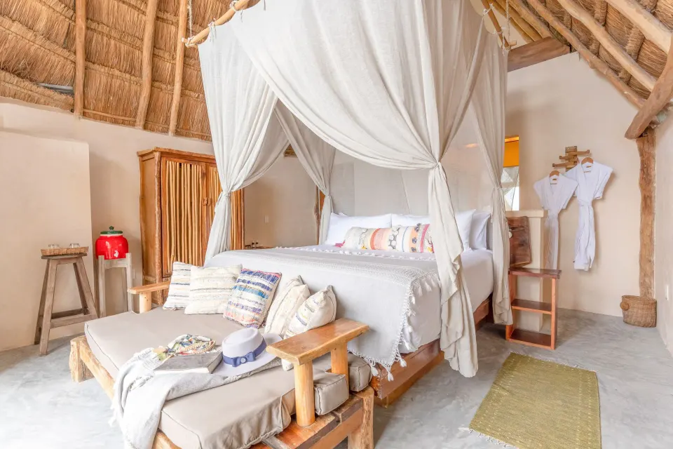 Canopy king bed under a thatched roof with seating bench at Ahau Tulum