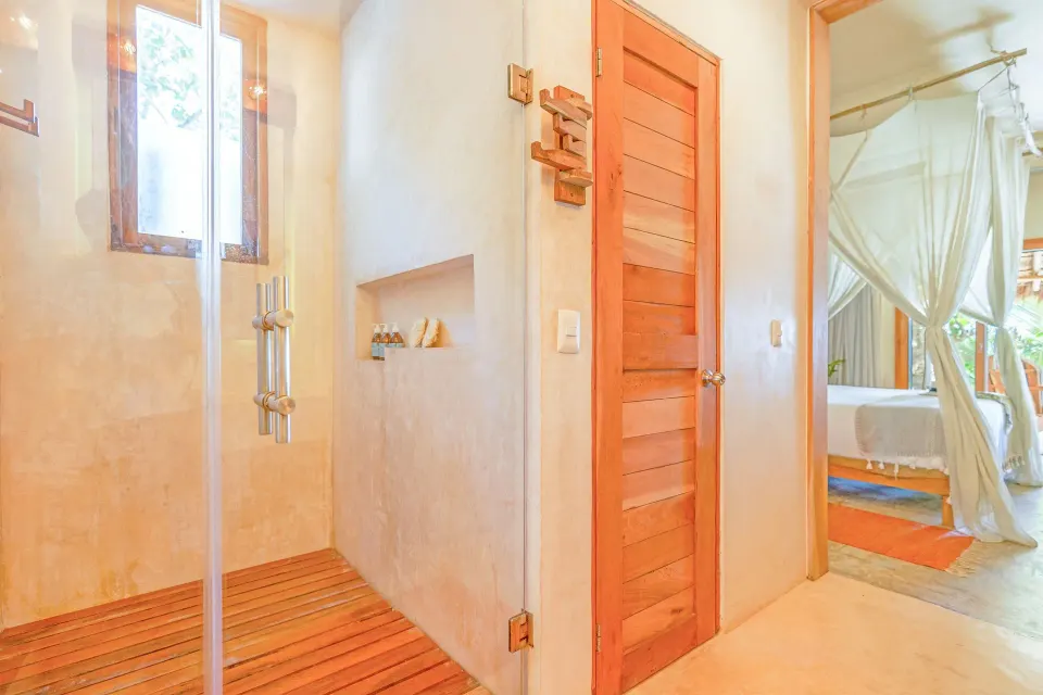 Junior Suite Oceanfront Beach level bathroom shower and wood-accented door at Ahau Tulum