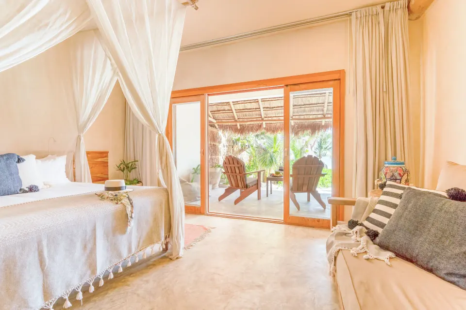 Junior Suite Oceanfront Beach level bedroom at Ahau Tulum with sofa and patio doors opening to greenery