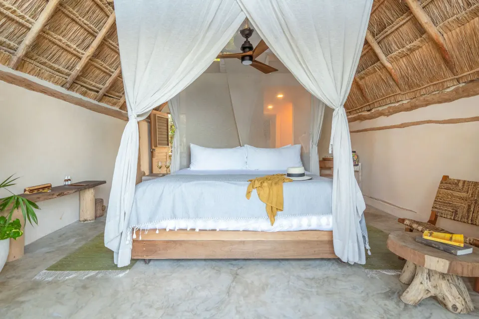 Front-facing view of a canopied king bed under a palapa ceiling in a Junior Suite at Ahau Tulum