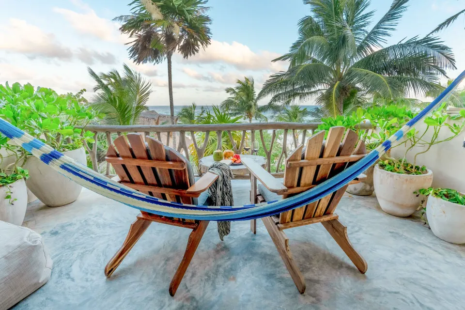 Balcony with wooden chairs and hammock overlooking palms and ocean at Ahau Tulum
