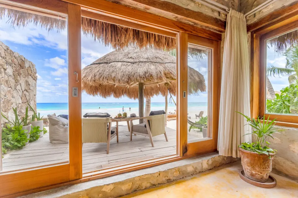 Sliding glass doors opening to a palapa-shaded deck and sea at Ahau Tulum