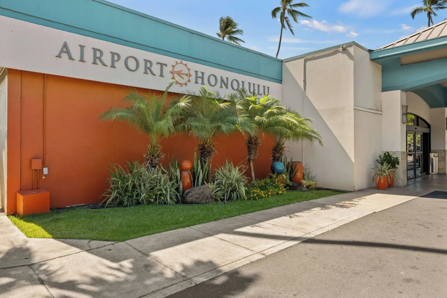 Angled exterior sign wall at Airport Honolulu Hotel with palms and entrance walkway.