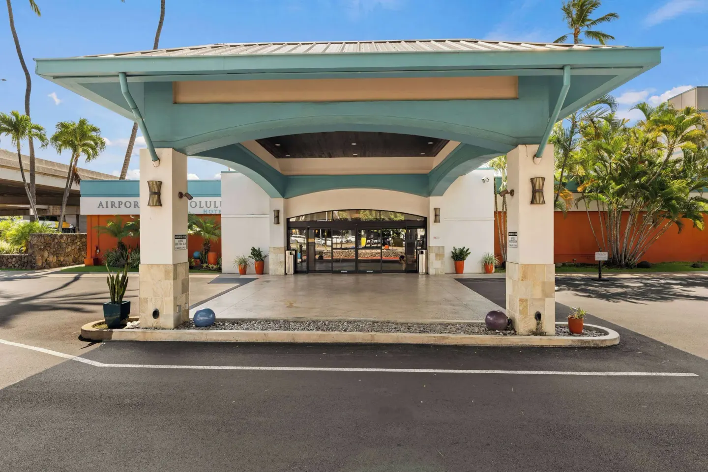 Covered entrance and driveway at Airport Honolulu Hotel with palms and glass doors.