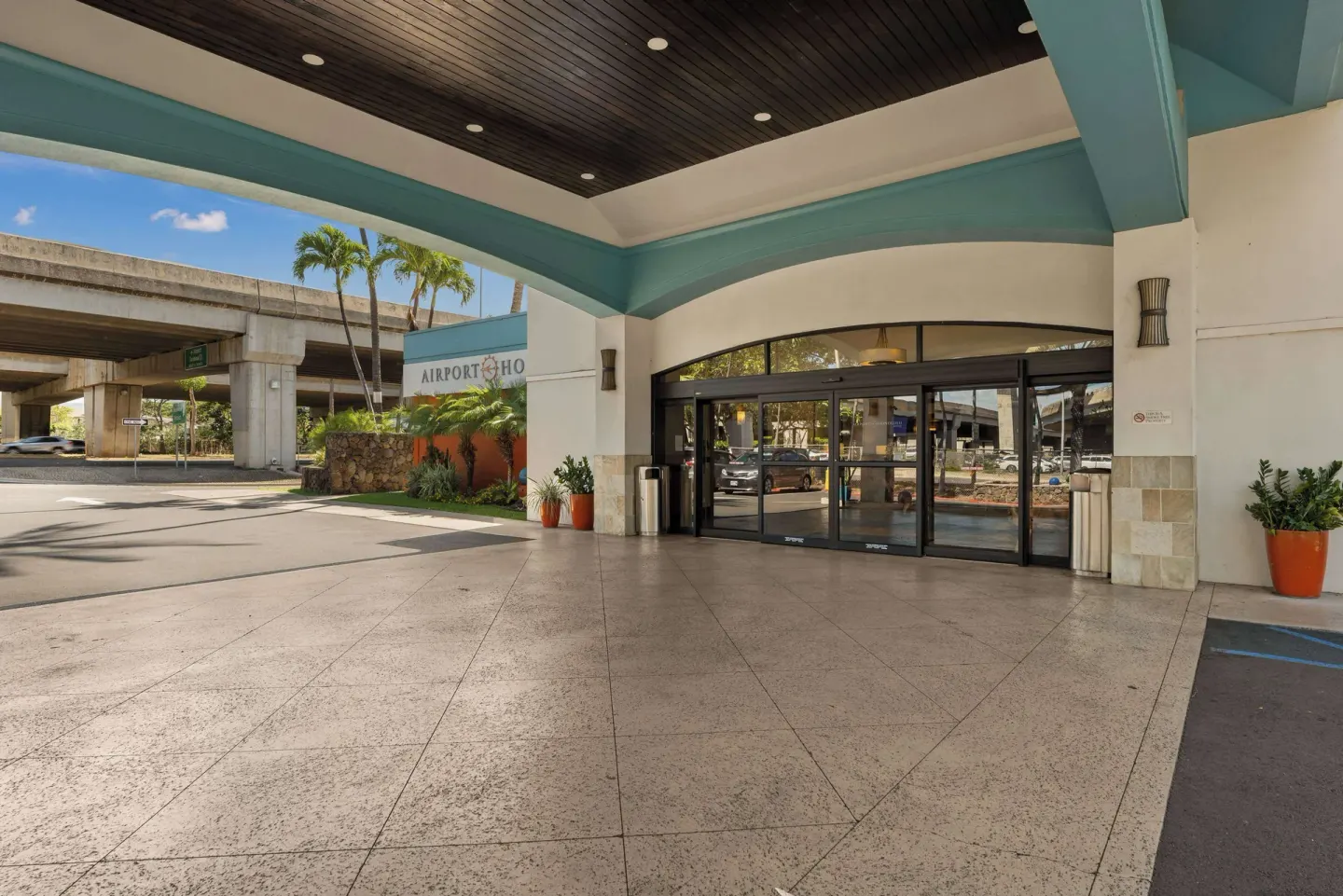 Hotel entry canopy at Airport Honolulu Hotel with sliding glass doors and nearby roadway.