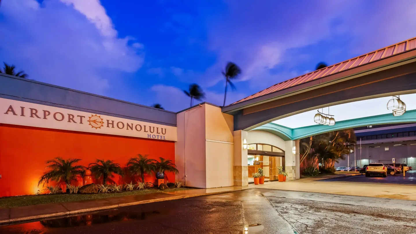 Evening hotel entrance with illuminated sign and porte cochere at Airport Honolulu Hotel.