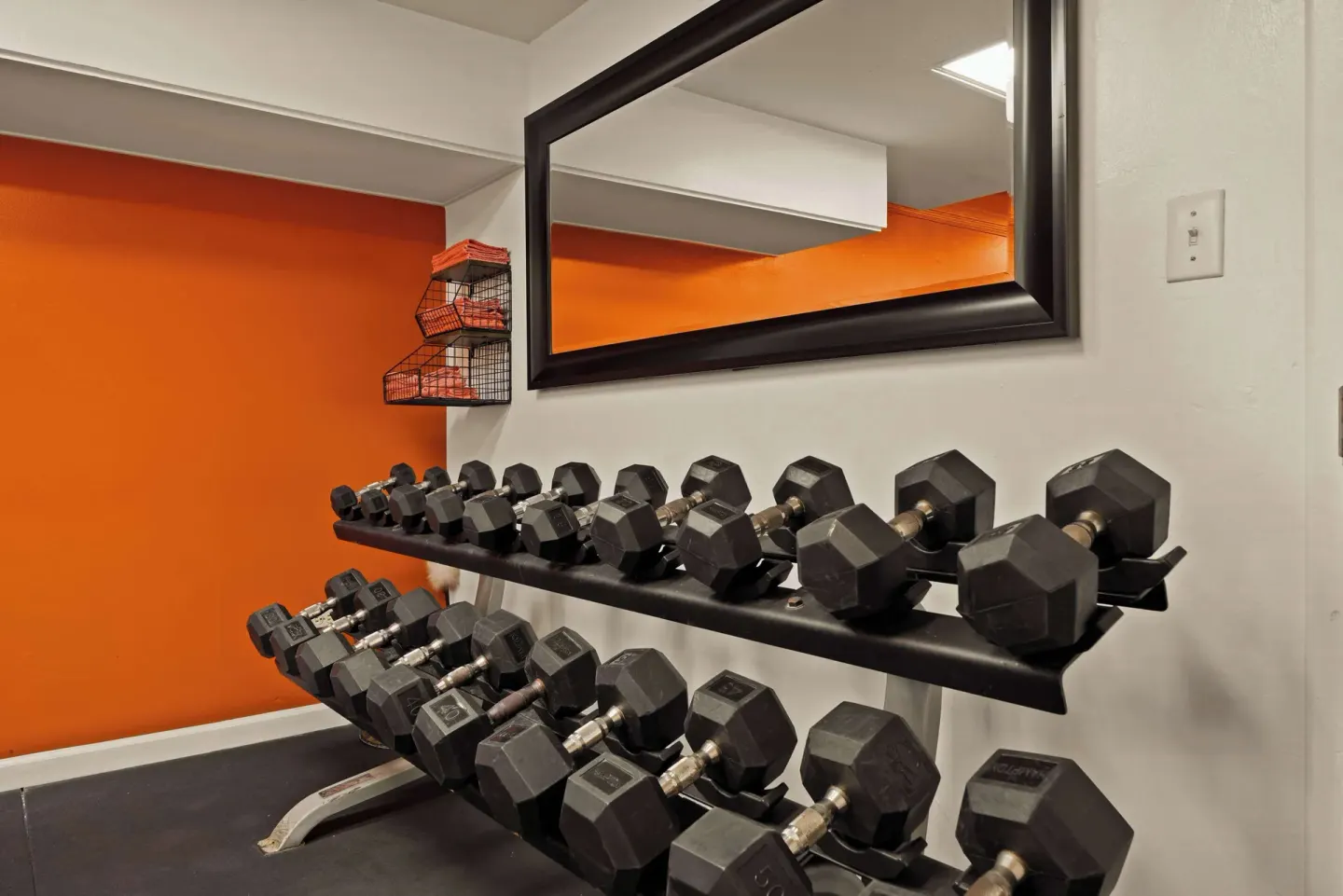 Dumbbells beneath a mirror with orange towels in the fitness room at Airport Honolulu Hotel.