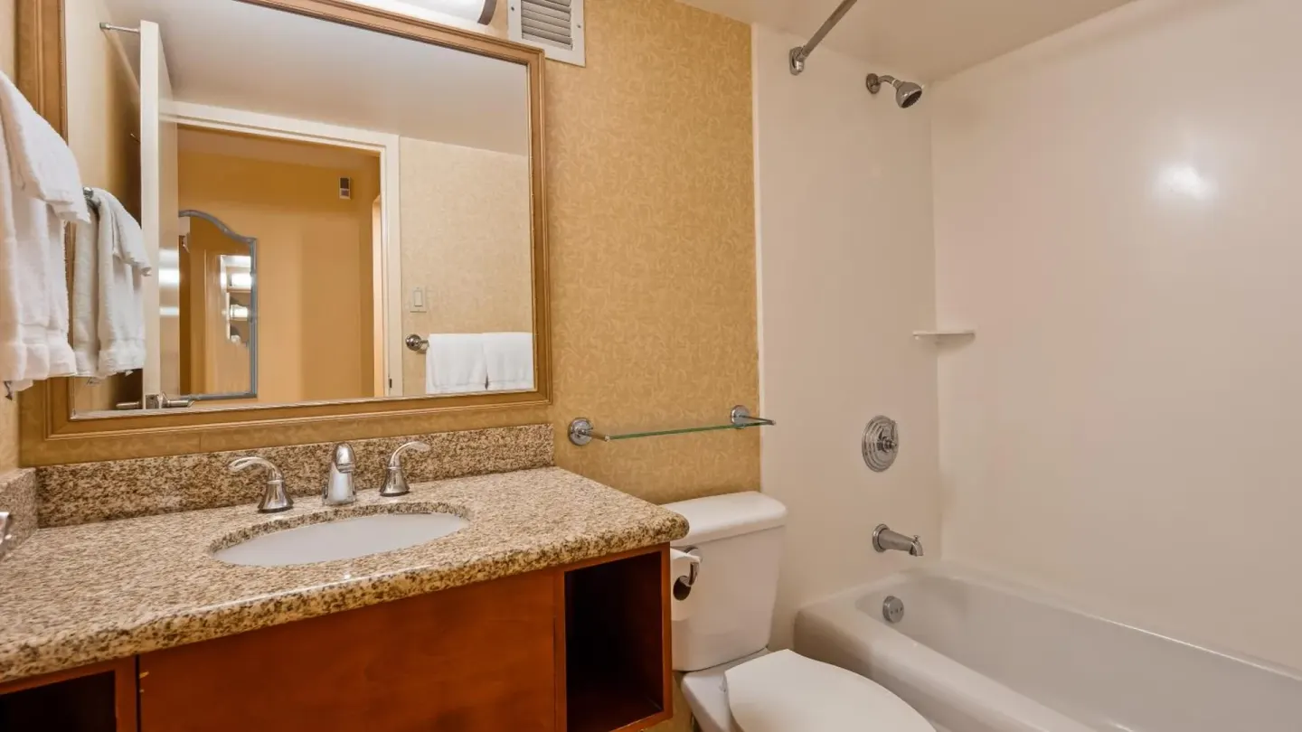 Guest bathroom with granite vanity and tub-shower at Airport Honolulu Hotel.