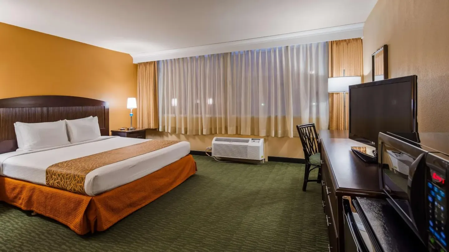 Guest room with a king bed, desk, TV, and curtained window at Airport Honolulu Hotel.
