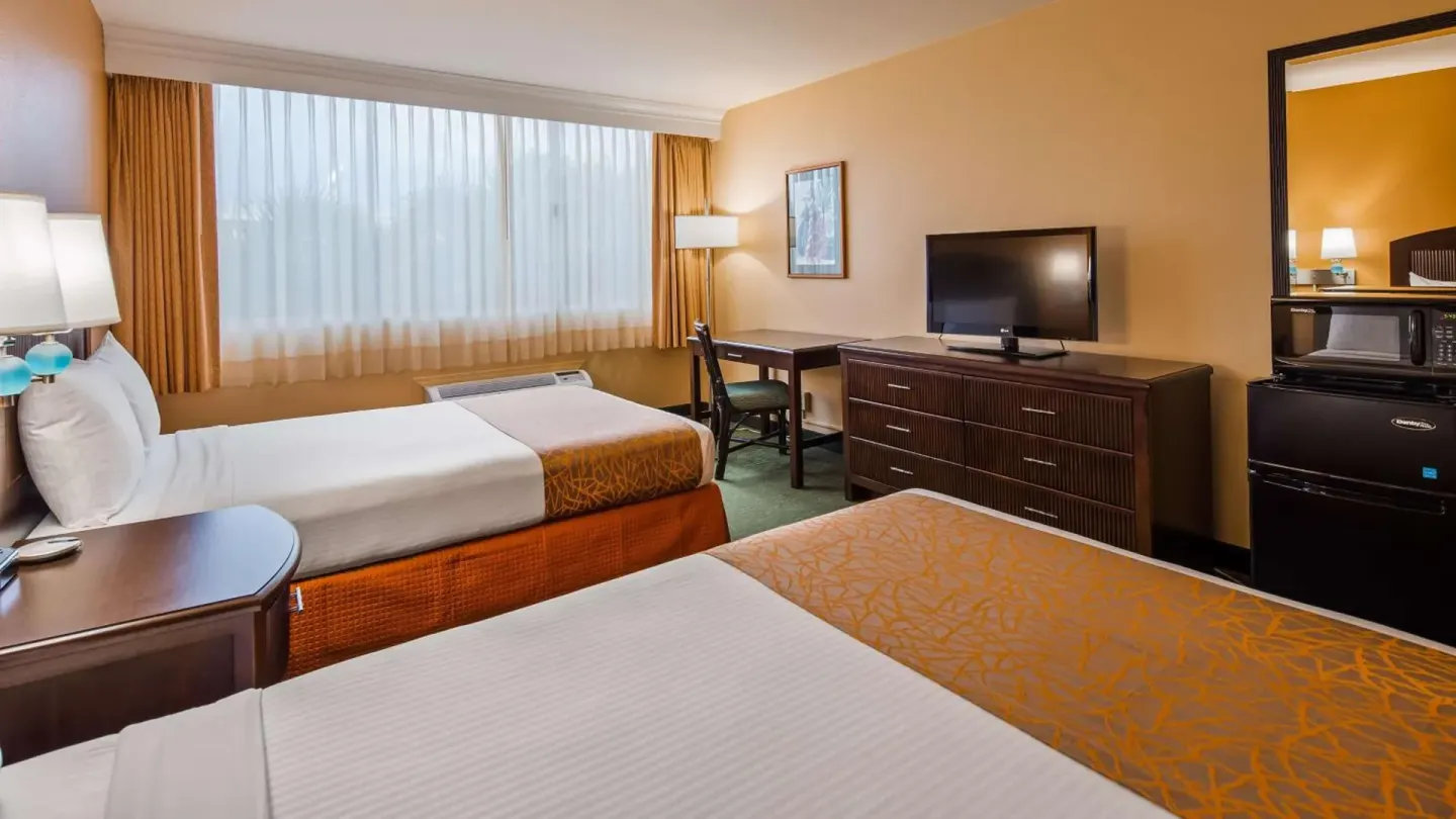 Two-bed guest room with dresser, TV, desk and mini fridge at Airport Honolulu Hotel.
