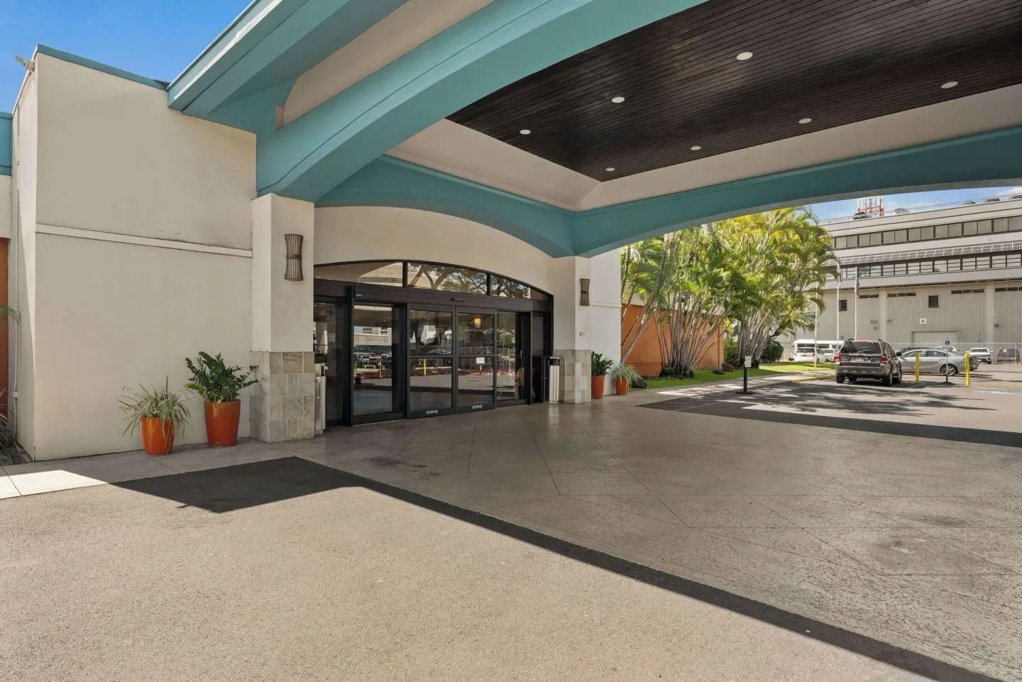 Side view of the covered entrance at Airport Honolulu Hotel with planters and parking area.