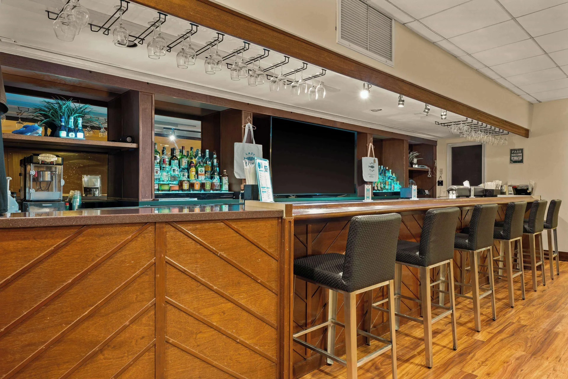 Bar counter with stools, bottle shelves, and hanging glassware at Airport Honolulu Hotel.