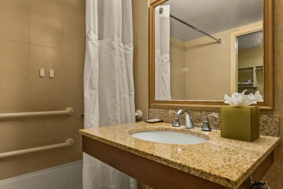 Bathroom vanity with sink, mirror and tub curtain at Airport Honolulu Hotel.