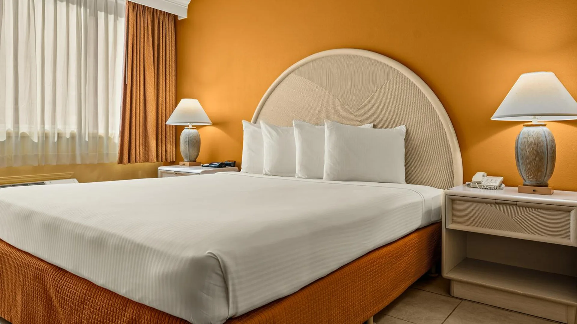 Non-smoking room with king bed and orange wall at Airport Honolulu Hotel.