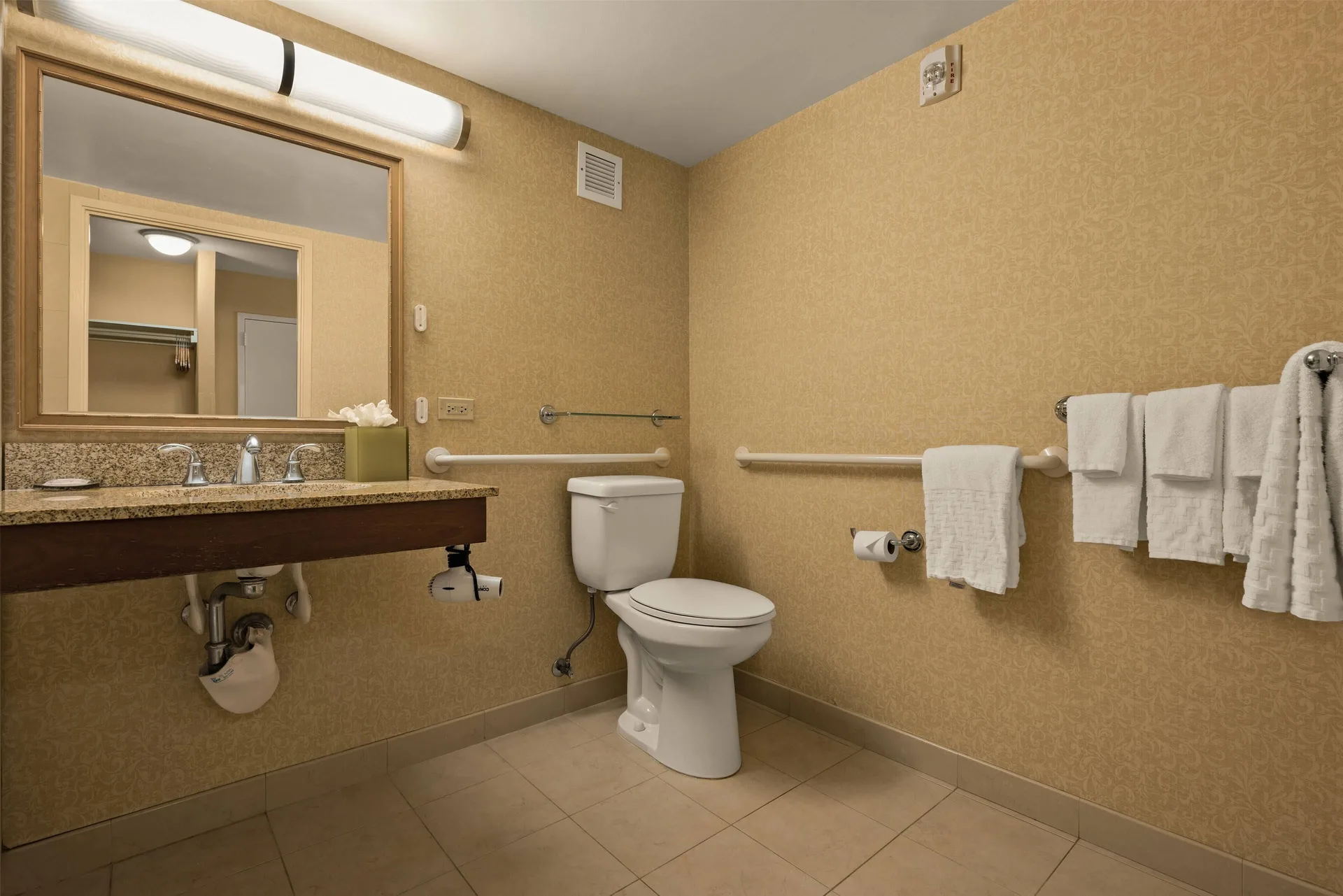 Accessible bathroom with vanity, toilet, grab bars, and towels at Airport Honolulu Hotel.