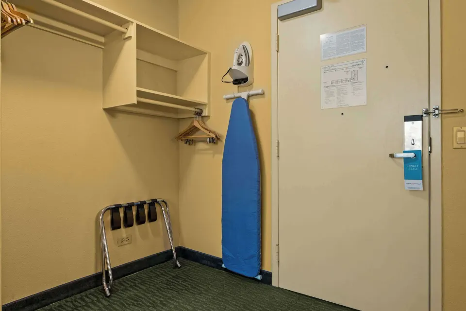 Guest room closet area with luggage rack, hangers, ironing board, and door at Airport Honolulu Hotel.