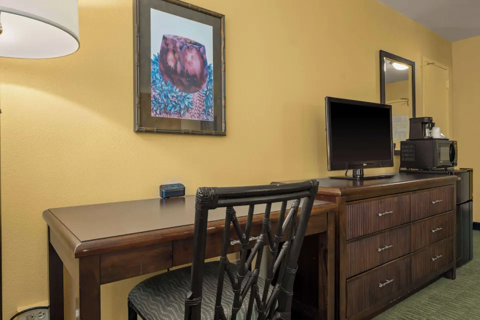 Guest room desk with chair, dresser, TV, microwave, and mini fridge at Airport Honolulu Hotel.