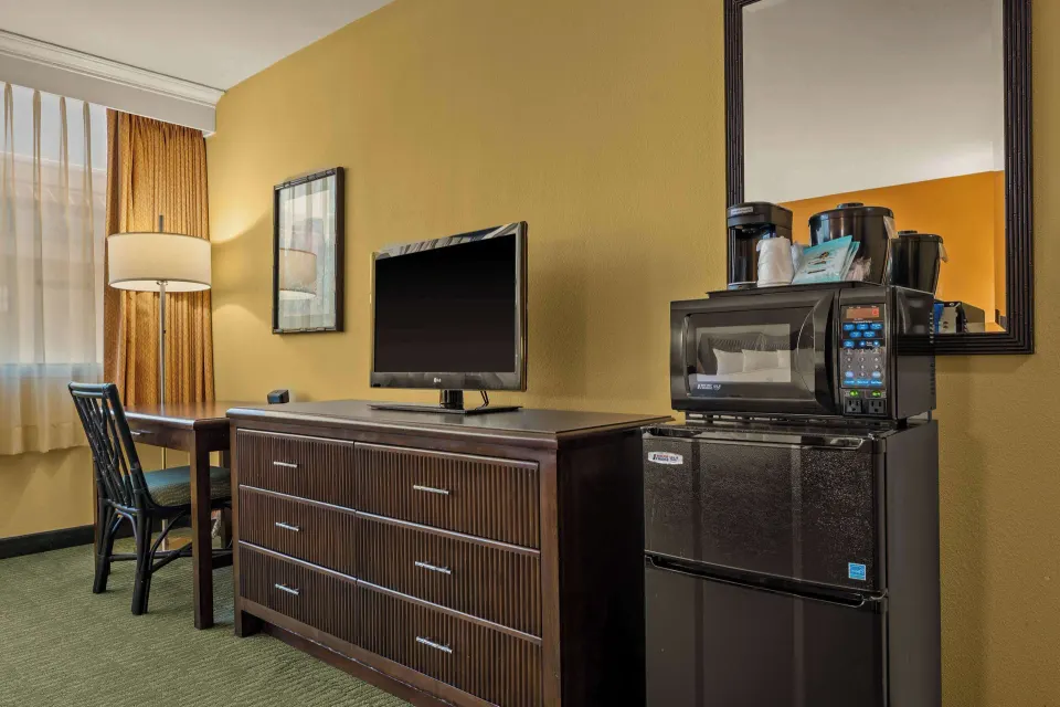 Guest room dresser with TV, microwave, mini fridge, coffee maker, and desk at Airport Honolulu Hotel.