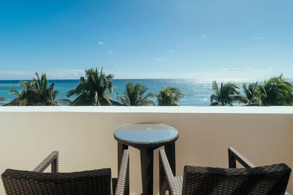 Ocean-facing balcony with two wicker chairs and small table at Akumal Bay Beach & Wellness Resort