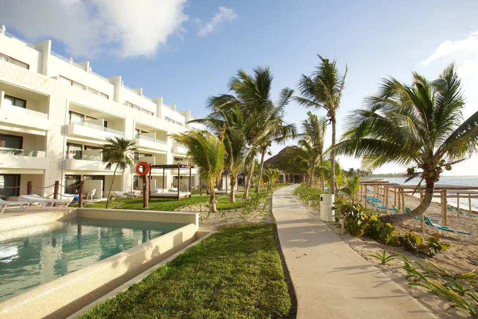 Resort pool and beachfront walkway with palm trees at Akumal Bay Beach & Wellness Resort