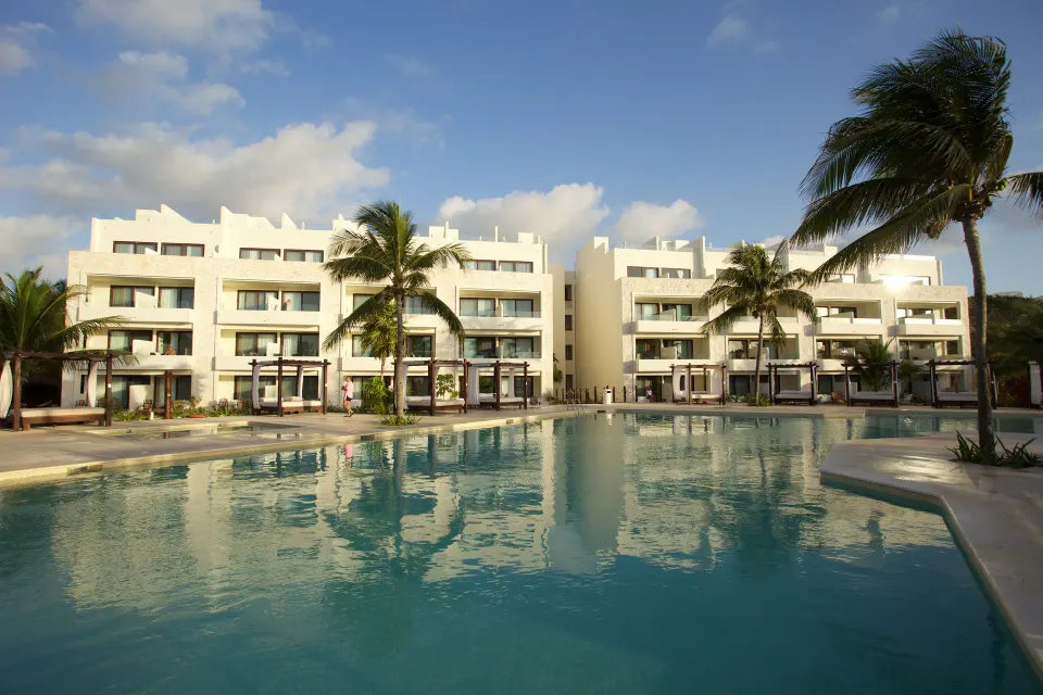 Large resort pool reflecting white multi-story buildings and palm trees at Akumal Bay Beach & Wellness Resort