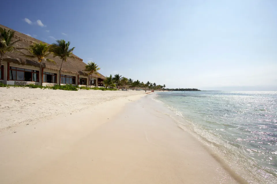 Wide sandy shoreline and thatched beachfront building at Akumal Bay Beach & Wellness Resort