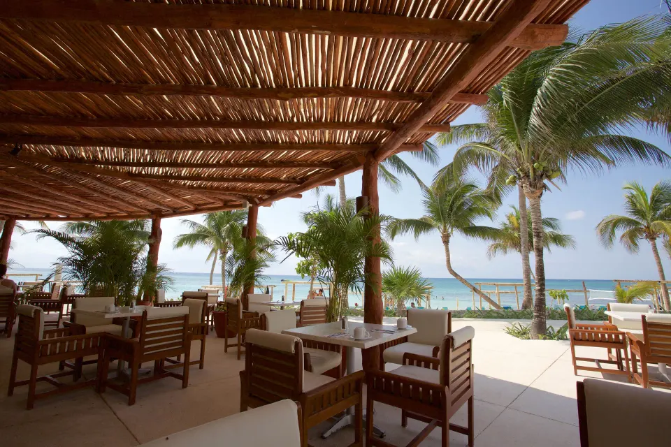 Open-air beachfront dining area with palapa roof at Akumal Bay Beach & Wellness Resort