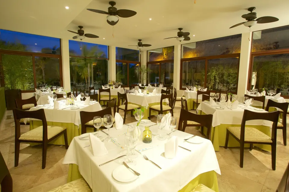 Indoor dining room set with white tablecloths and glassware at Akumal Bay Beach & Wellness Resort