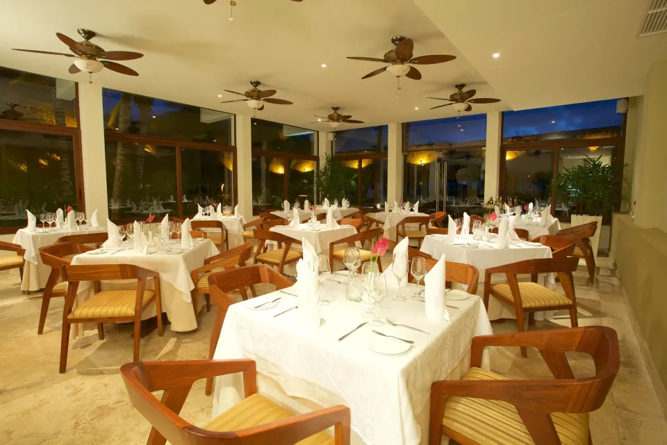Bright indoor dining room with white linens and ceiling fans at Akumal Bay Beach & Wellness Resort