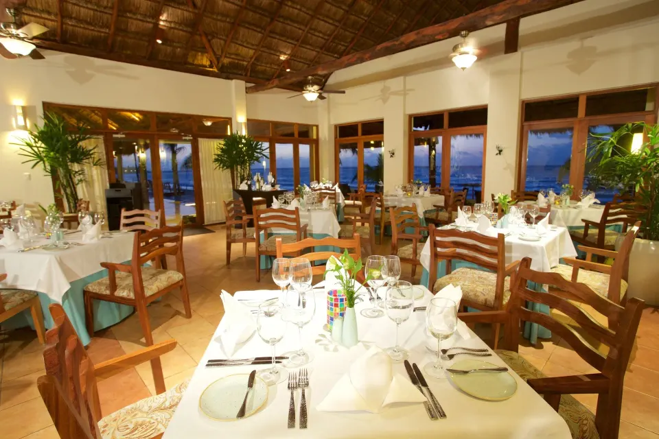 Thatched-roof seaside restaurant dining area set with plates and glasses at Akumal Bay Beach & Wellness Resort