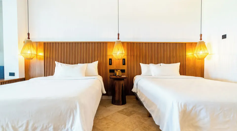 Two twin beds with wood slat headboard and hanging lamps in a Junior Suite at Akumal Bay Beach & Wellness Resort