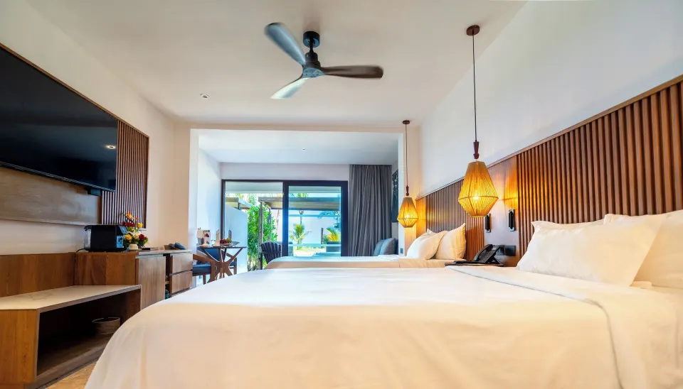 Two beds and pendant lights facing patio in a Junior Suite at Akumal Bay Beach & Wellness Resort