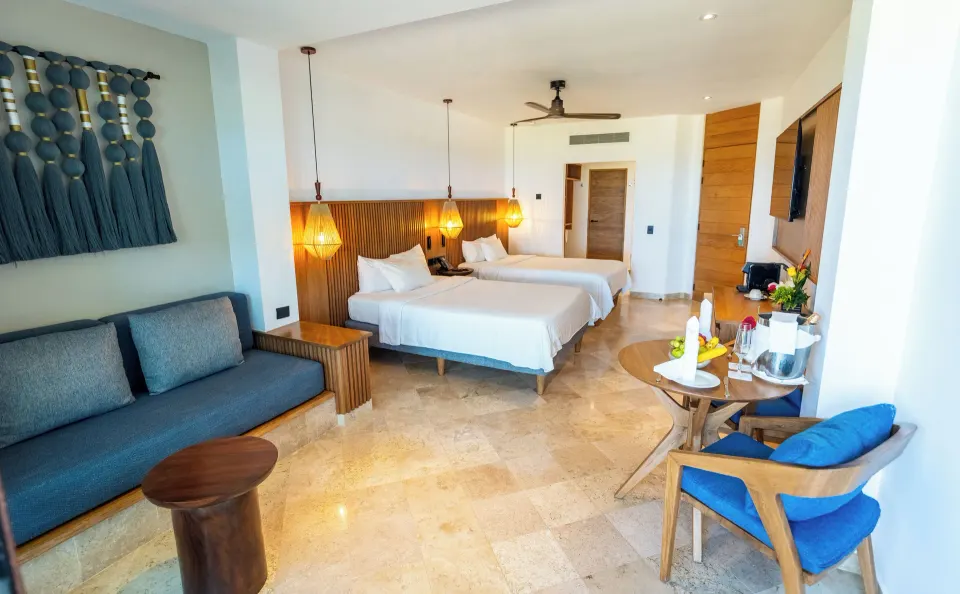 Wide view of a Junior Suite interior with seating area, two beds and patio at Akumal Bay Beach & Wellness Resort