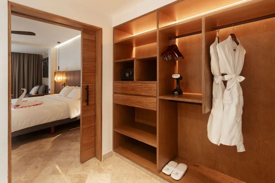 Open closet and robe with view into the bedroom of a Junior Suite at Akumal Bay Beach & Wellness Resort
