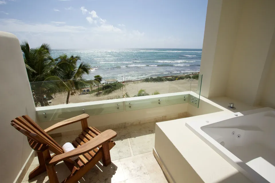 Balcony with wooden chairs and a jacuzzi overlooking the ocean at Akumal Bay Beach & Wellness Resort