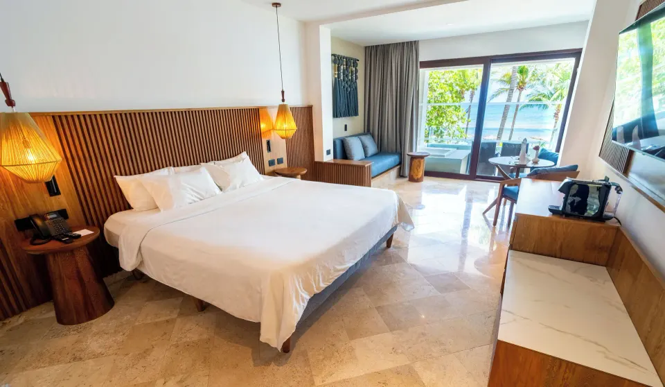 Junior Suite king bed and seating area with ocean view through glass doors at Akumal Bay Beach & Wellness Resort