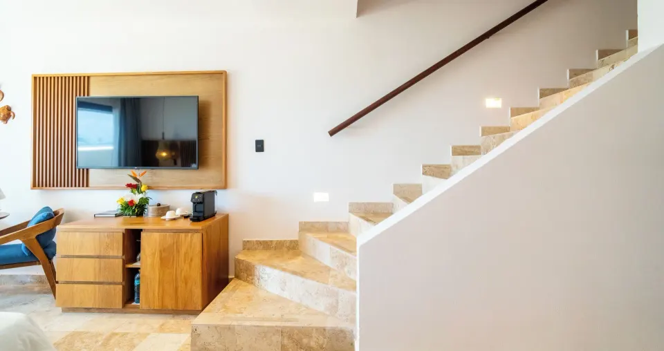 Interior of junior suite with staircase, TV and wooden dresser at Akumal Bay Beach & Wellness Resort