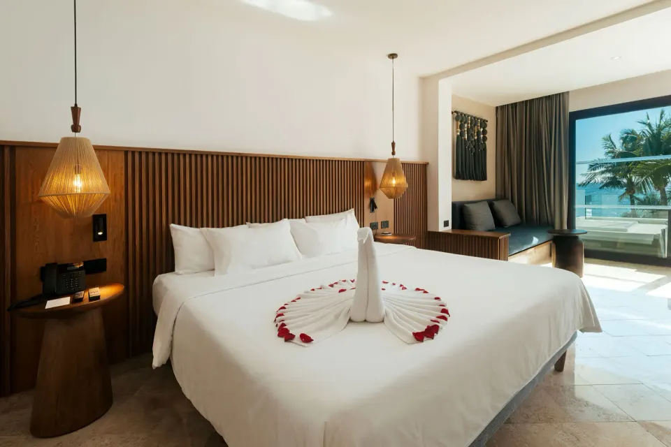 King bed with decorative towel and ocean view in a Junior Suite at Akumal Bay Beach & Wellness Resort