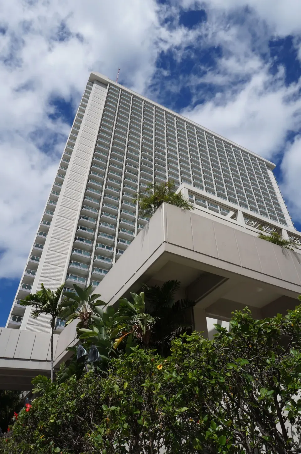Low-angle view of Ala Moana Hotel tower with balconies above landscaping.