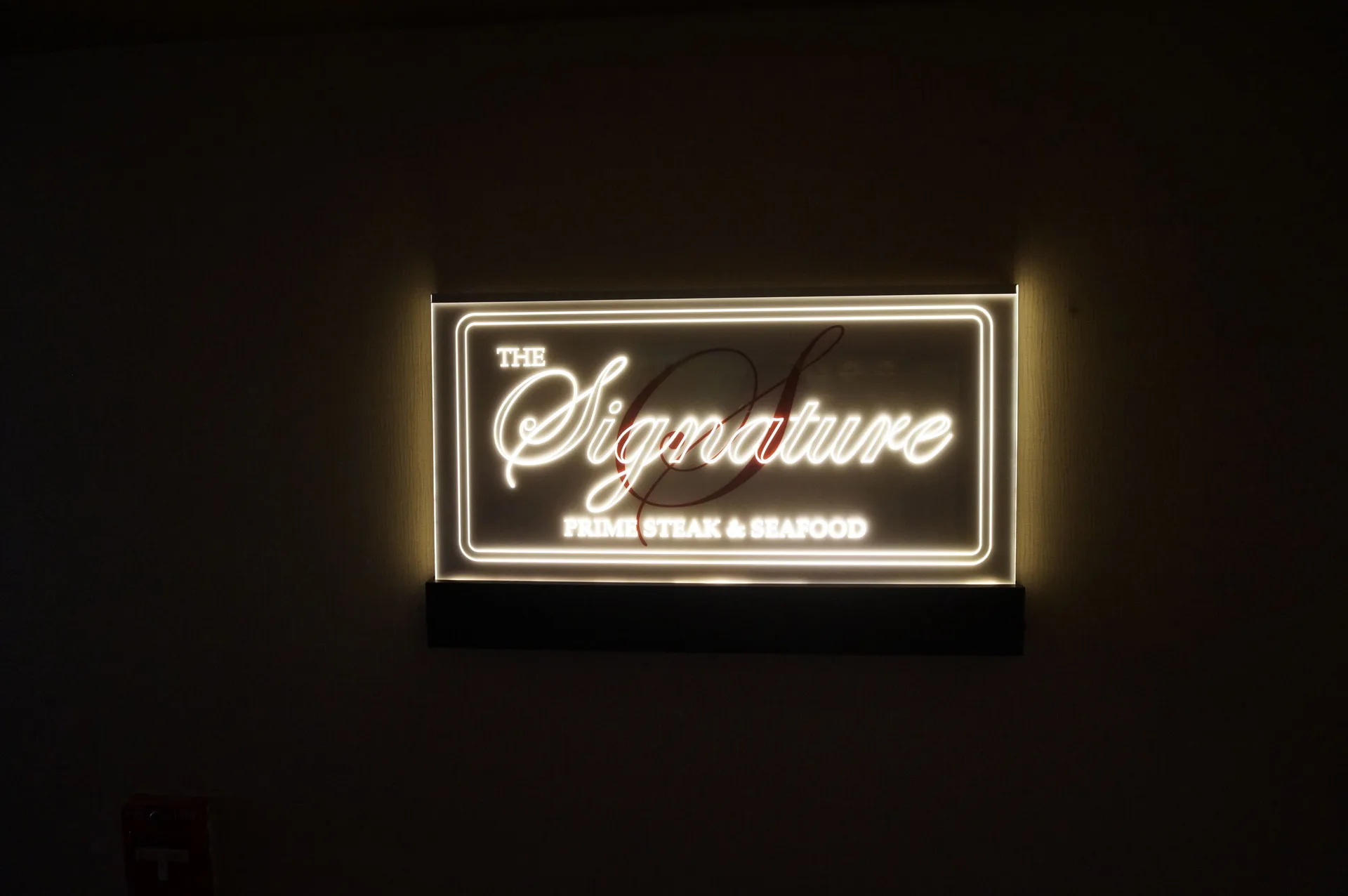 Illuminated Signature Prime Steak & Seafood sign on a dark wall at Ala Moana Hotel.