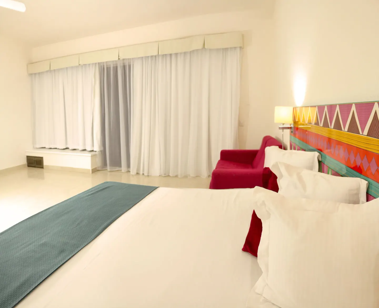 Guest room bed with colorful headboard and red chair at All Ritmo Cancun Resort & Water Park.